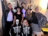 Foto: Sieben Mitarbeitende in Helloween-Kostümen: Fünf stehen, zwei sitzend davor.