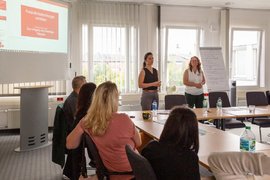 BTZ-Psychologinnen referieren stehend vor einem Whiteboard bei der Agentur für Arbeit. Vor ihnen sitzend Zuhörerinnen an einem Tisch.