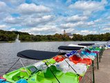 Foto: Sommerwetter am See. Bunte Tretboote, teils mit Überdachung am Ufer. 
