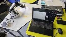 Foto: Blick auf einen Schreibtisch mit Laptop, mit der der danebenstehende Roboterarm gesteuert wird.