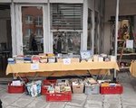 Foto des Bücherflohmarktes auf dem Ostermarkt. Abgebildet ist ein langer Tisch, auf dem Bücher gestapelt liegen. Darunter befinden sich rote und graue Kisten, ebenfalls gefüllt mit Büchern.