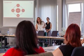 BTZ-Psychologinnen referieren stehend vor einem Whiteboard bei der Agentur für Arbeit. Vor ihnen sitzend zwei Zuhörerinnen an einem Tisch.