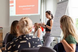 BTZ-Psychologinnen referieren vor einem Whiteboard bei der Agentur für Arbeit. Vor ihnen sitzend Zuhörer*innen an einem Tisch.