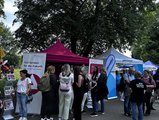 Foto: Beratungsstände mit bunten Zelten, Menschen informieren sich zu Bildung und Beruf. Banner und Broschüren weisen u. a. auf Jobcenter-Angebote hin.