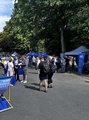 Foto: Besucher*innen und Ausstellende im Gespräch vor den Informationszelten. Bäume umgeben die Messefläche.