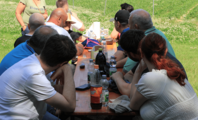 Foto: Auf dem Foto sind Personen zu sehen, die an einer Biertischgarnitur sitzen. Im Hintergrund sieht man das Erdbeerfeld. Auf dem Tisch stehen Getränke.