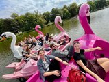 Gruppenfoto: BTZ-Mitarbeiter*innen beim fröhlichen Ausflug auf dem Teich.  Je drei Personen sitzen in drei Flamingo-Tretbooten und einem Schwanen-Tretboot. 