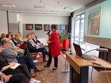 Galeriebild: Frau mit Mikrofon spricht mit den Besucher*innen der Tagung.