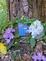 Gebastelte blaue Holztür am Fuße eines Baumes. Davor bunte Blumen am Waldboden