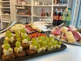 Catering zum Eröffnungstag: Platten mit Käse-Trauben-Spieße, Tomaten, belegte Baguette sowie im Hintergrund Getränke.