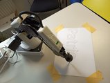 Foto von oben auf den Roboterarm, der gerade etwas schreibt. 
