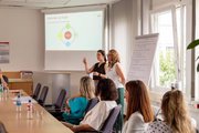 Zwei Referentinnen stehend vor Whiteboard und Zuhörer*innen.