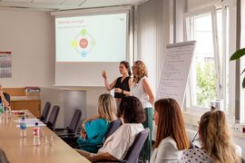 Zwei Referentinnen stehend vor Whiteboard und Zuhörer*innen.