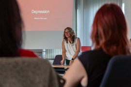 BTZ-Psychologin referiert stehend vor einem Whiteboard bei der Agentur für Arbeit. Vor ihr sitzen Zuhörer*innen an einem Tisch.