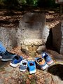 fünf einzelne Wanderschuhe stehen am Bellmanns Brunnen. Ein Wanderer streckt seinen Fuß mit Schuh ins Bild