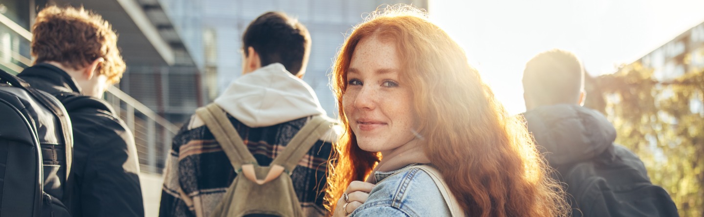 Symbolbild Autismus: Eine junge Frau läuft hinter einer Gruppe junger Männer und blickt zurück in die Kamera
