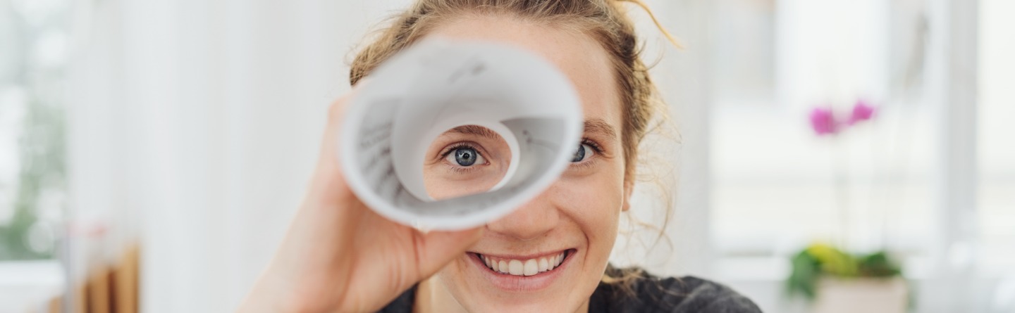 Symbolbild Sucht: Eine Frau blickt durch ein zusammengerolltes Papier wie durch ein Teleskop