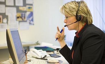 Frau mit Headset sitzt am PC und telefoniert