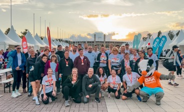 Gruppenfoto der Läuferinnen und Läufer mit DAK-Maskottchen im Sonnenuntergang.