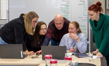 Foto: Vier Ergotherapeutinnen lassen sich von einem Ergotherapeuten etwas am Laptop erklären.