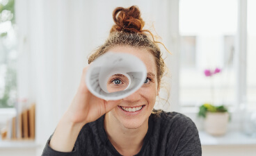 Junge Frau sieht durch ein zum Fernrohr zusammengerolltes Papier. 