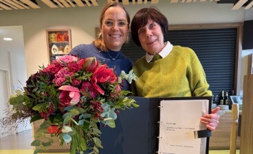 Verabschiedung: Zwei Personen stehen, Frau Grimmer, Leiterin des BTZ Jena, übergibt einen Bluemnstraß an Ulrike Klöppel. Ulrike Klöppel steht daneben und hält ein Abschiedsbuch in der Hand.