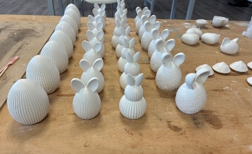 Foto: Gips-Dekorohlinge in verschiedenen Ausführungen für Ostern (Eier u. Hasen), ordentlich aufgereiht auf einem Holztisch.