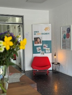 Foto vom Eingangsbereich des BTZ-Neuro Kamen mit Roll-Up der faw , einem roten Sessel und im Vordergrund eine Blumenvase.