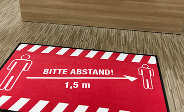 Rote Fußmatte mit weißer Schrift Abstand 1,5 m.