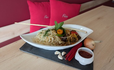 Asiatische Rindfleischpfanne mit Mie-Nudeln Foto: Auf einem hellen Holztisch steht ein appetitlich angerichtetes Gericht: asiatische Rindfleischpfanne mit Mie-Nudeln.
