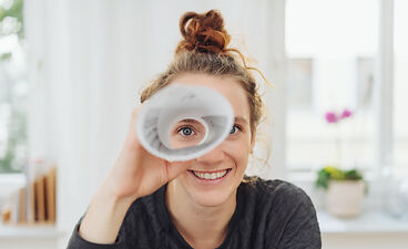 Beispielfoto: Eine Frau schaut durch eine Papierrolle wie durch ein Fernglas in die Kamera.