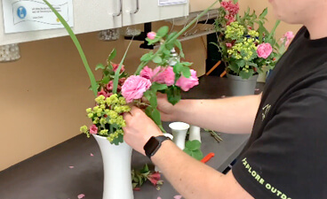 Teaserbild: Hände verteilen Blumen in einer Vase