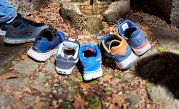 5 einzelne Wanderschue der Wanderer stehen am Bellmanns Brunnen. Ein Wanderer streckt seinen Fuß mit Schuh ins Bild