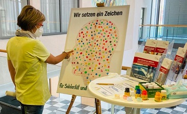 Teaserbild: Eine Frau hinterlässt mit Farbe ihren bunten Fingerabdruck auf der Leinwand